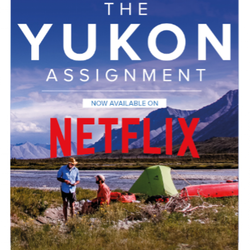 Yukon Assignment Film Poster - two men are camping on a riverbank with a mountain in the background