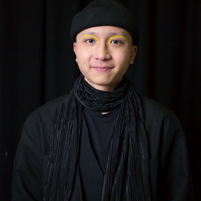 Student portrait - an Asian man wears a black beanie, a black top and a black scarf