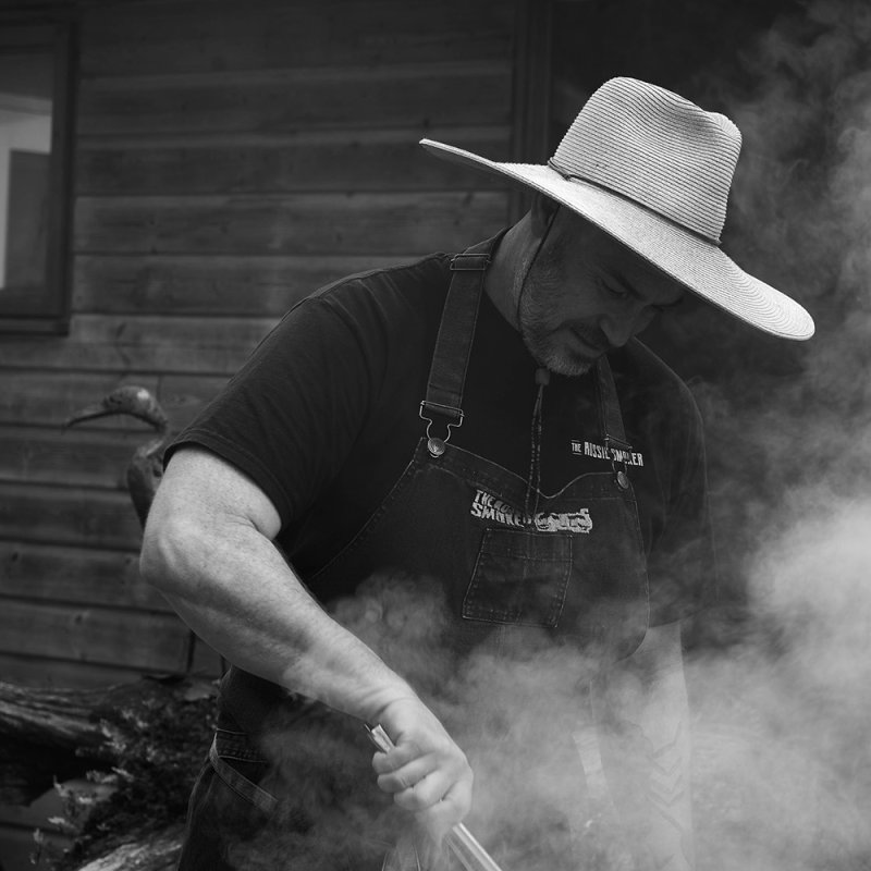 Black and white photo of a man wearing a wide brim hat at a bbq