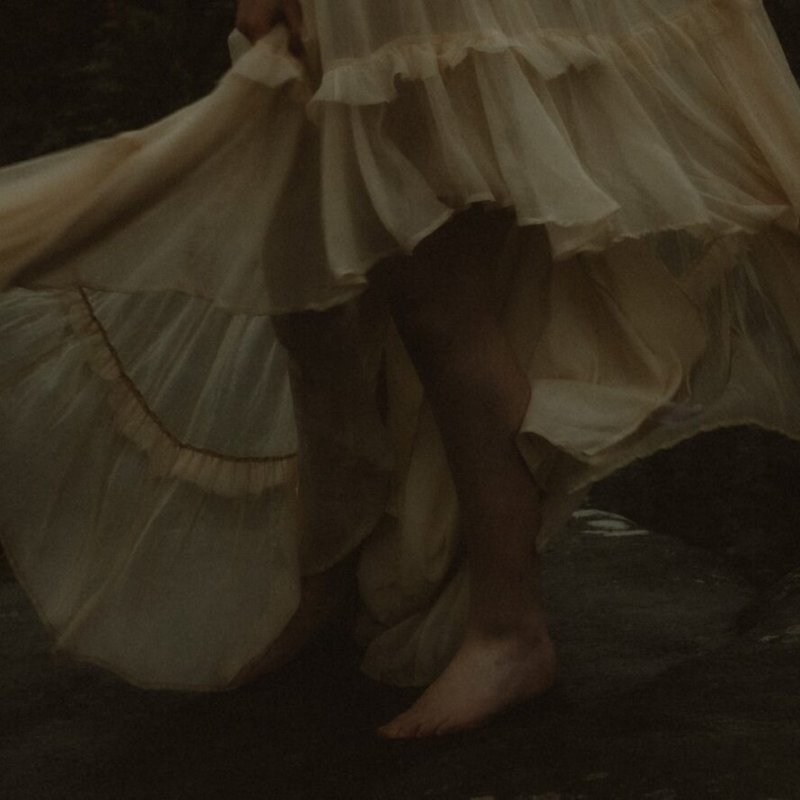 The feet and legs of a woman standing on a rock wearing a floaty dress