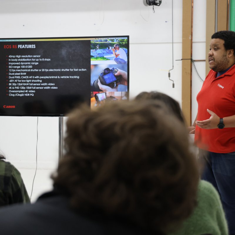 A man wearing a red t-shirt, doing a presentation on a screen