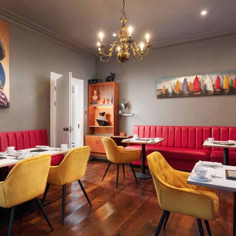 Dining space at Chelsea House in Falmouth. Red booth-style seating, gold chandelier, mustard velvet chairs, wooden flooring 