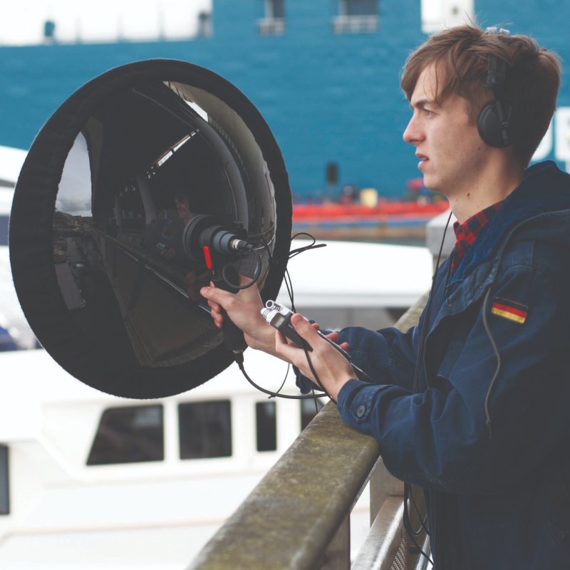 Student holding large recording device and wearing headhpones outside in Falmouth