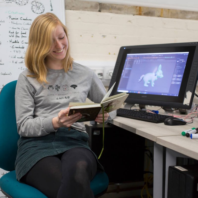 Student looking at book next to drawing tablet