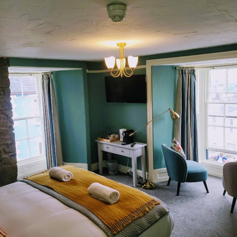 A double room at Jacob's Ladder - exposed stone and teal walls, white bed sheets with mustard and grey blankets, two seats facing out towards a large window.