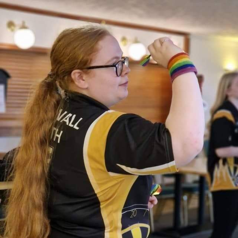 A girl with long red hair holing a dart near her face