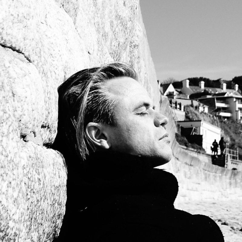 A man reclines against a stone wall. Black and white image
