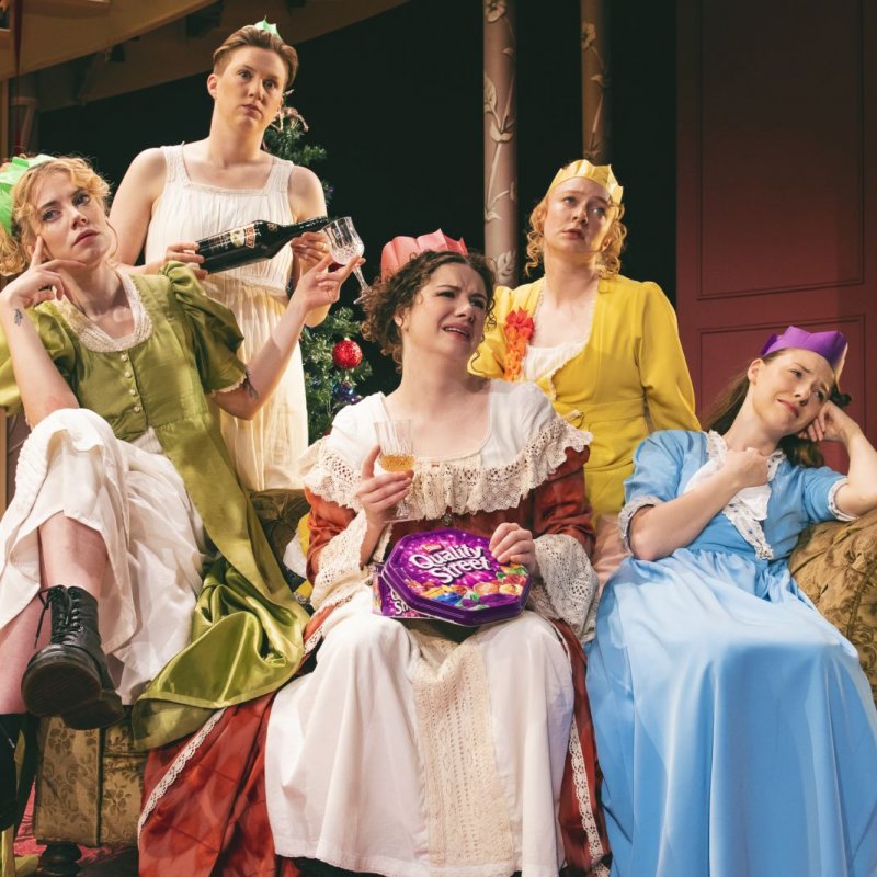 Five women sit on a sofa, looking glum and eating quality street