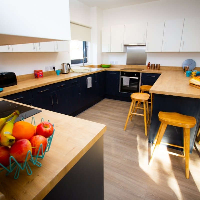 A student kitchen equipped with toaster, kettle, microwave, table, chairs and an oven