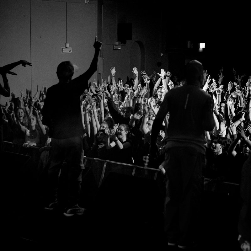 Three people performing on a stage facing a large crowd with their hands in the air