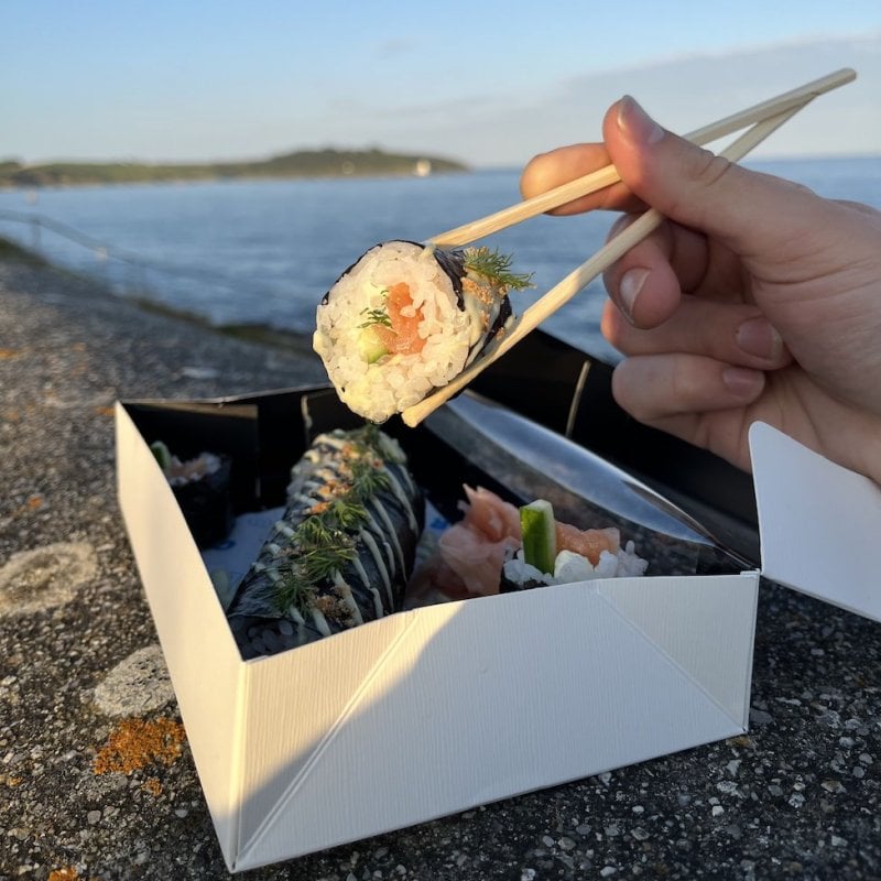 A hand holding chopsticks picking up sushi from a box