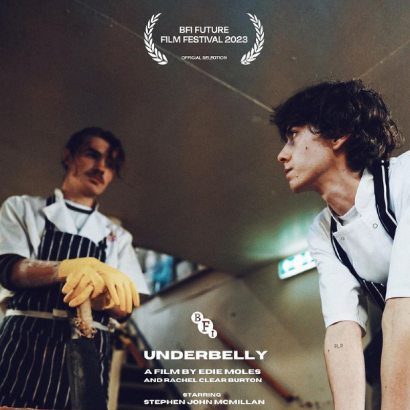 Two butchers looking at each other intensely in a kitched. Text reads: BFI Future Film Festival 2023, Underbelly, A film by Edie Moles and Rachel Clearn Burton, starring Stephen John McMillan