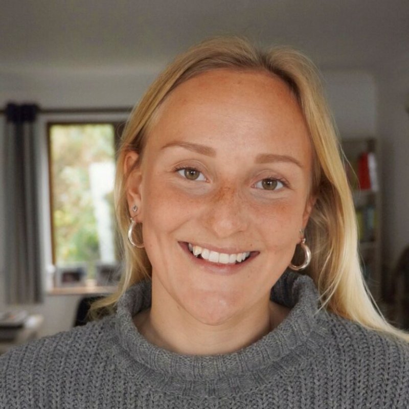 A blonde haired woman wearing a grey jumper smiles 