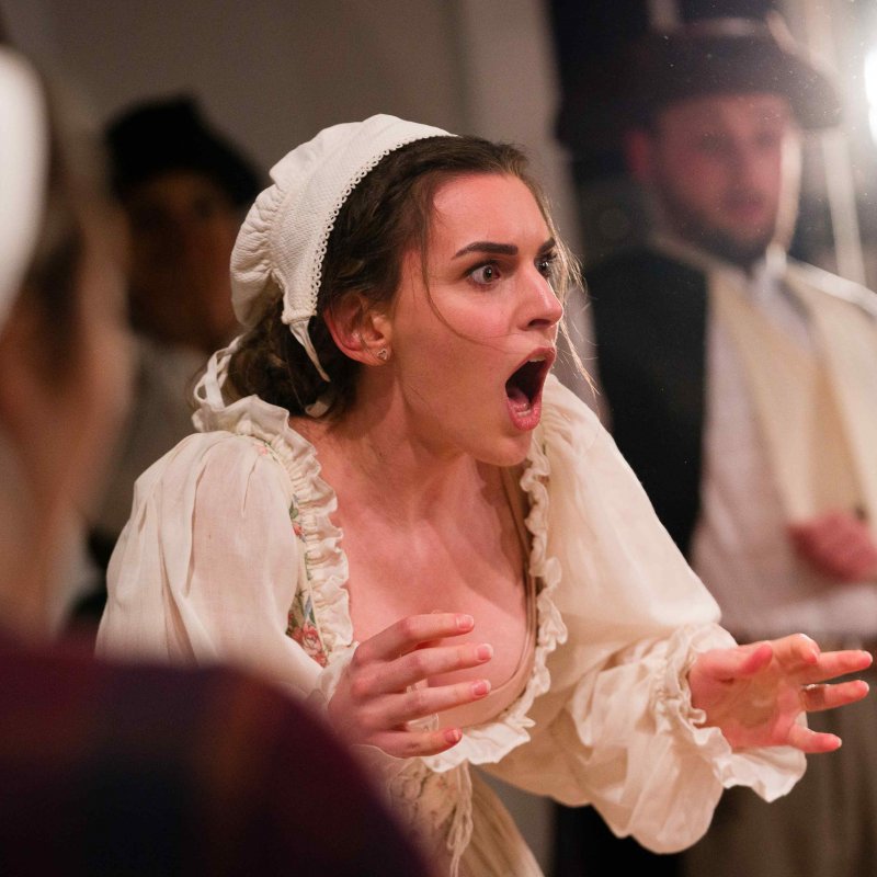 A woman dressed as a maid has a shocked expression on her face