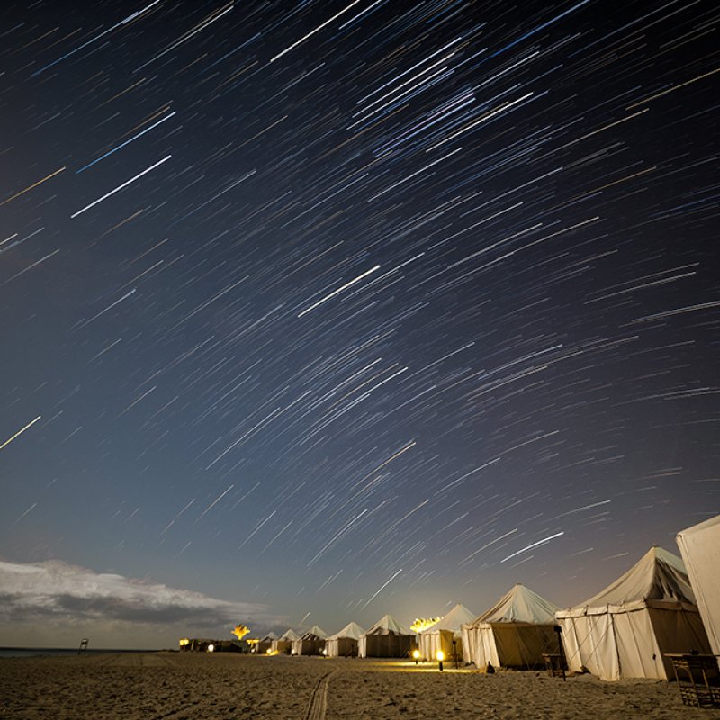 Photo of white tents on the beach in Egypt with light trails of stars overhead.