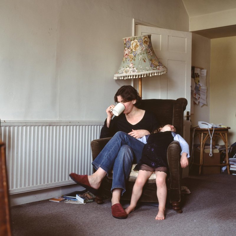 Photograph of a woman sat in a chair with a young child leaning back