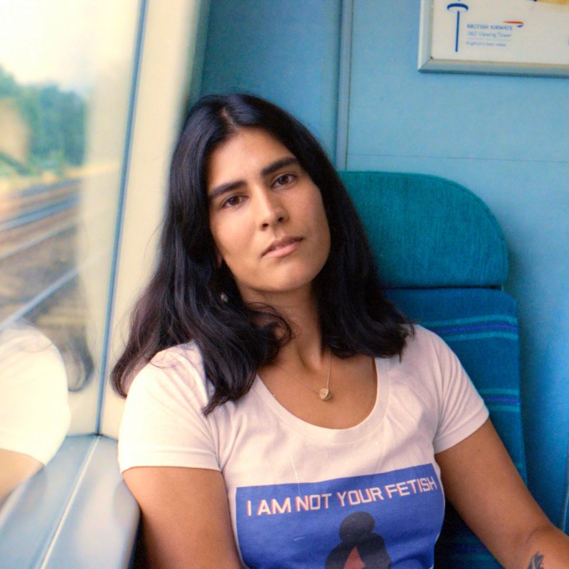 Photo of a woman leaning against the window of a train, looking into the camera.