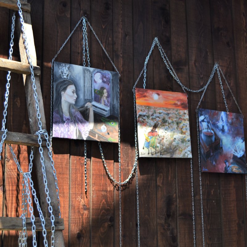 Some painted canvases hanging up on a wooden wall with chains connecting them
