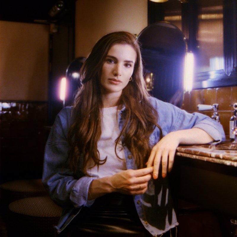 Photo of a woman sat at a bar looking into the camera.