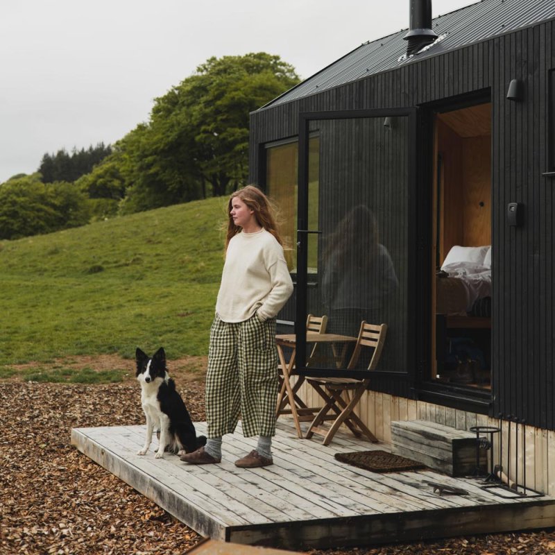 A young woman and a collie outside a cabin
