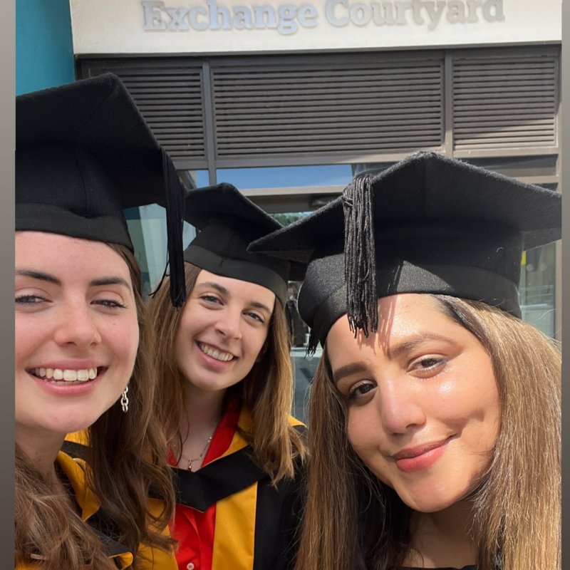 Three women wearing graduation gowns pose together 