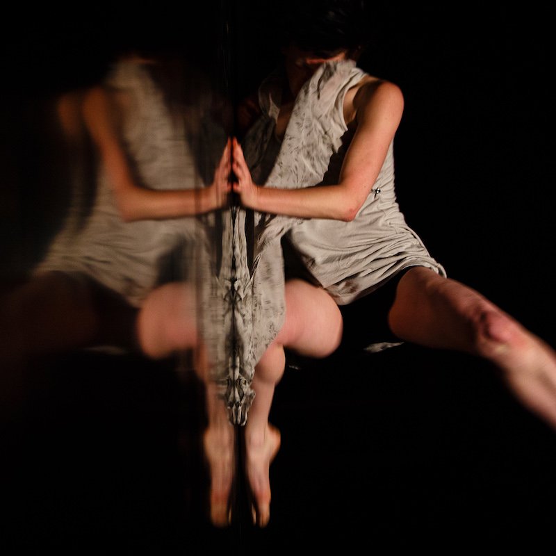 Dance reflecting in dark shiny surface, leg stretched out.