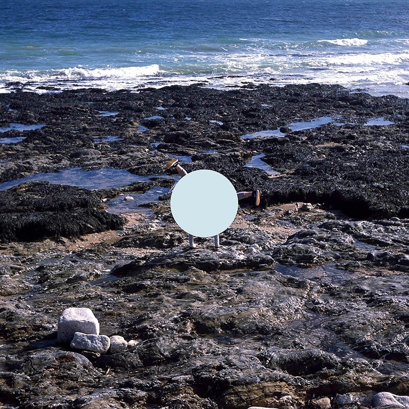 Photo of someone doing a handstand amongst rock pools, with blue sea in the background. A light blue circle is covering the person so that only arms and legs are showing.