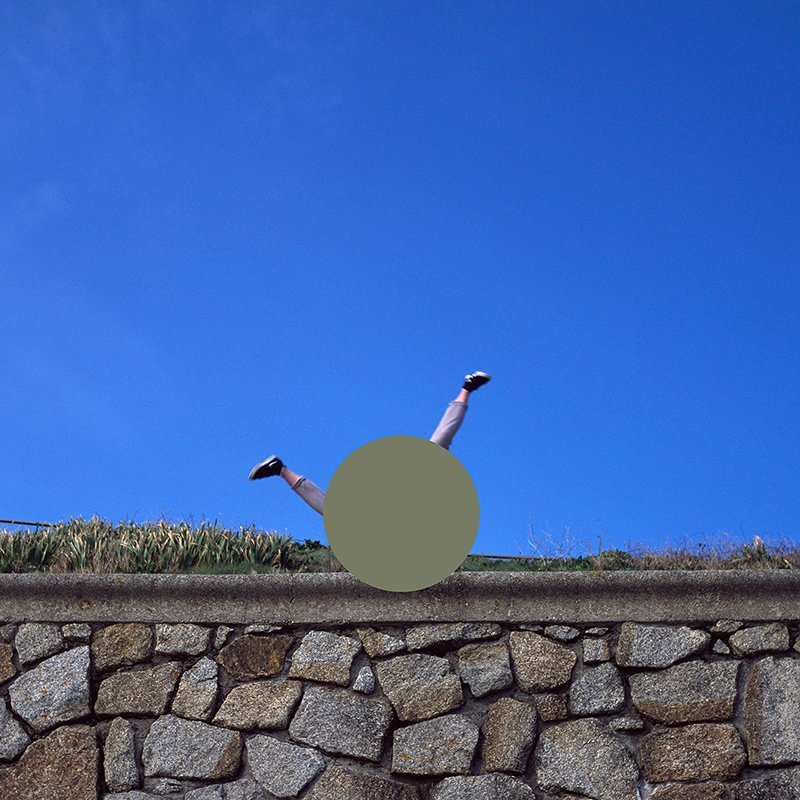 Photo of someone doing a handstand on stone wall, with green grass and blue sky in the background. A grey circle is covering the person so that only arms and legs are showing.