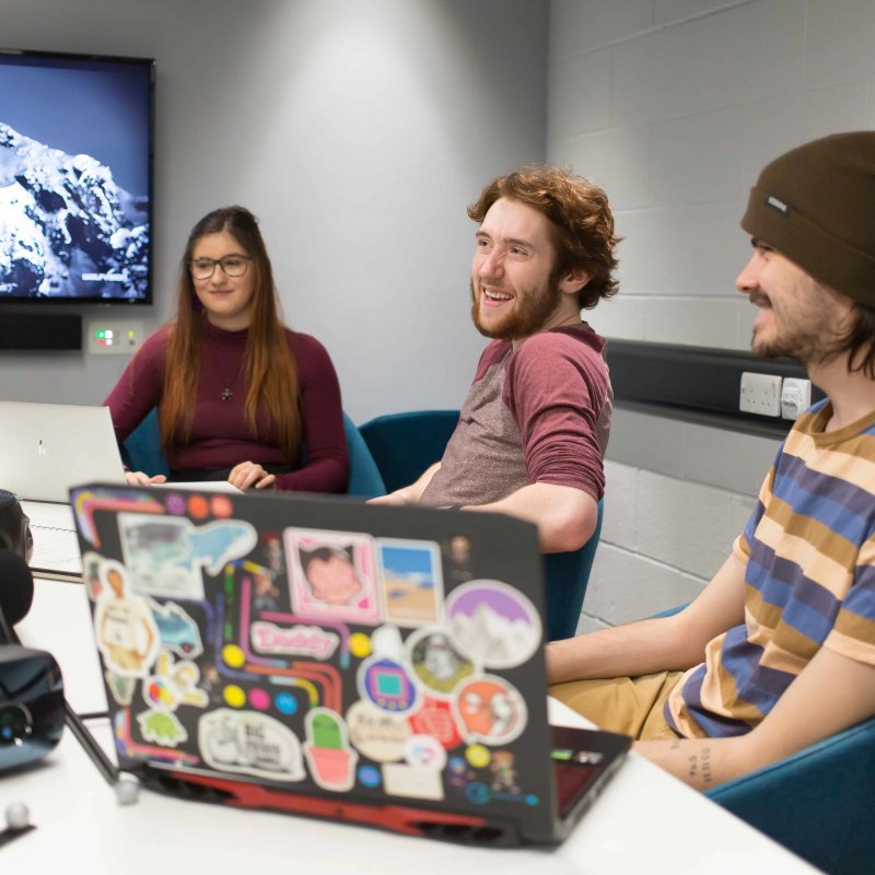 Three Falmouth Univesity students sitting at a table with open laptops