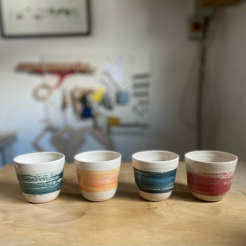 Four ceramic cups in a row, each a different colour. Here we have dark green, light orange, dark blue and dark red