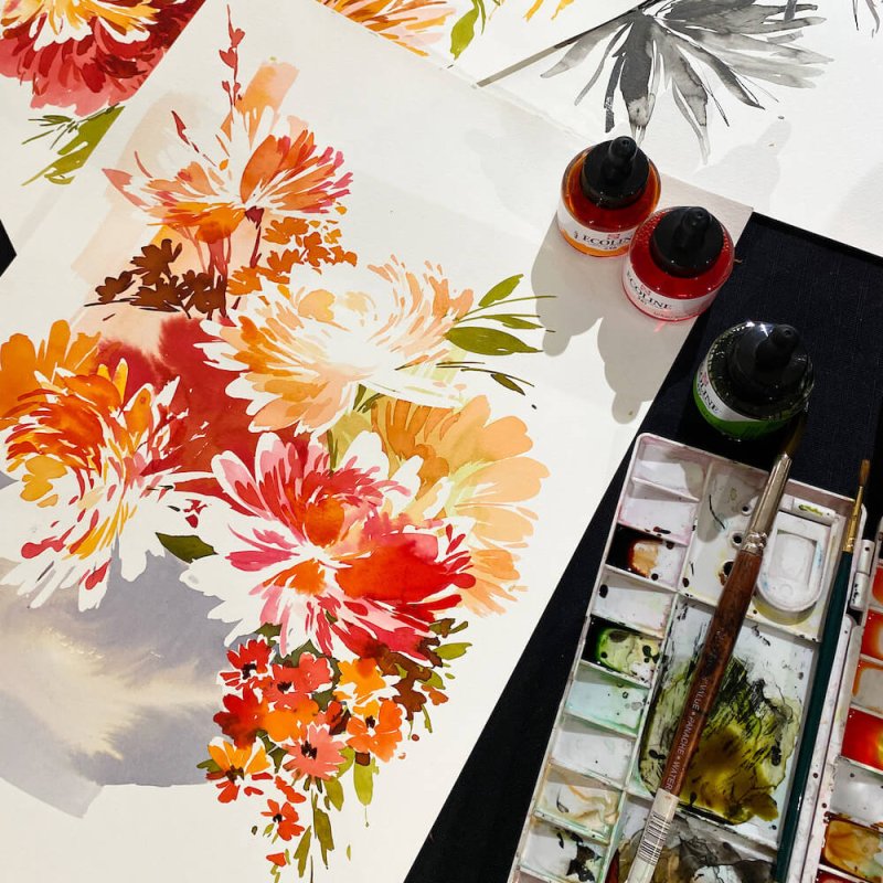 A watercolour sketch of red and orange flowers next to a watercolour pallet