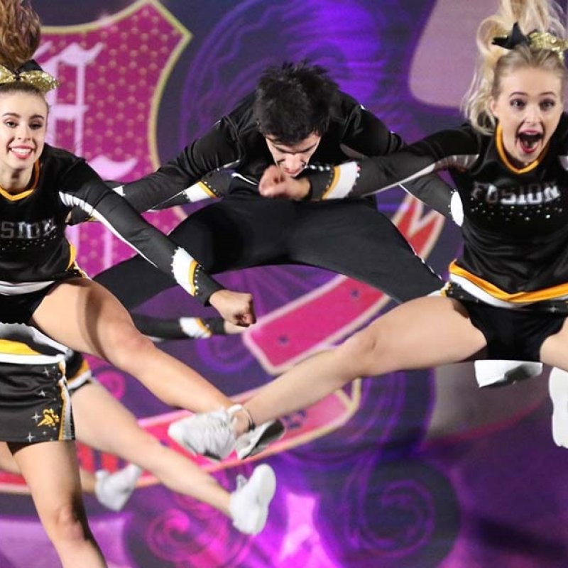 Photo of cheerleaders wearing black and yellow uniforms doing the splits in the air.