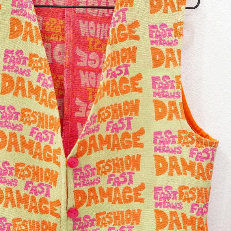 Red, orange and yellow waistcoat with woven text 'fast fashion means fast damage'