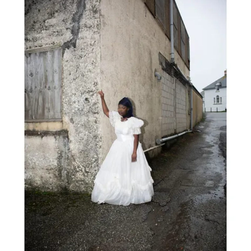 Cornish girl wearing white prom dress leaning against a wall down an alleyway - from Cornish Maids photography project by Fran Rowse