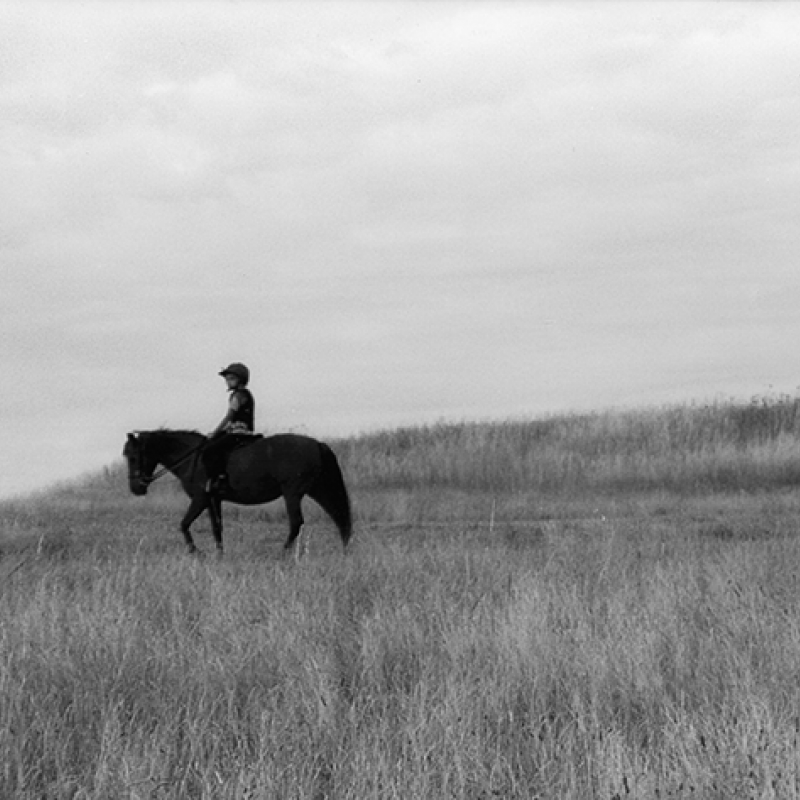 Black and white image of a person riding a horse