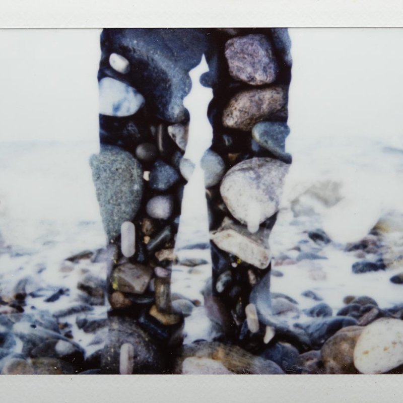 Polaroid of legs overlayed with stones on a beach
