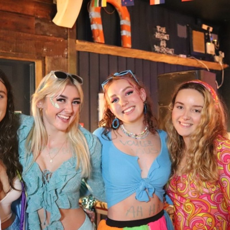 Four smiling girls wearing colourful 70s and 80s style clothing at a bar
