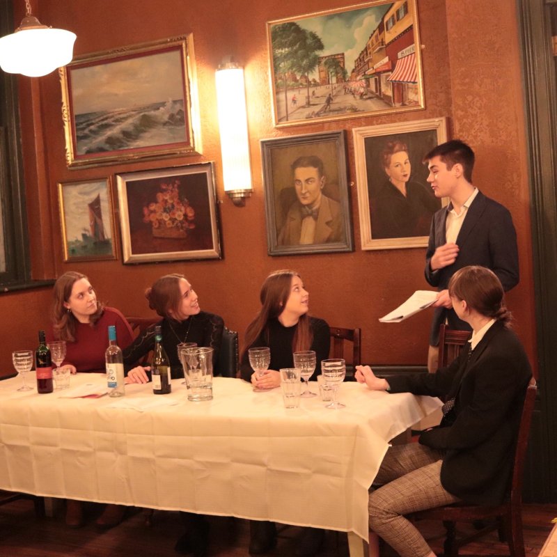 Five people wearing formal attire sat at a table in a Victorian styled room