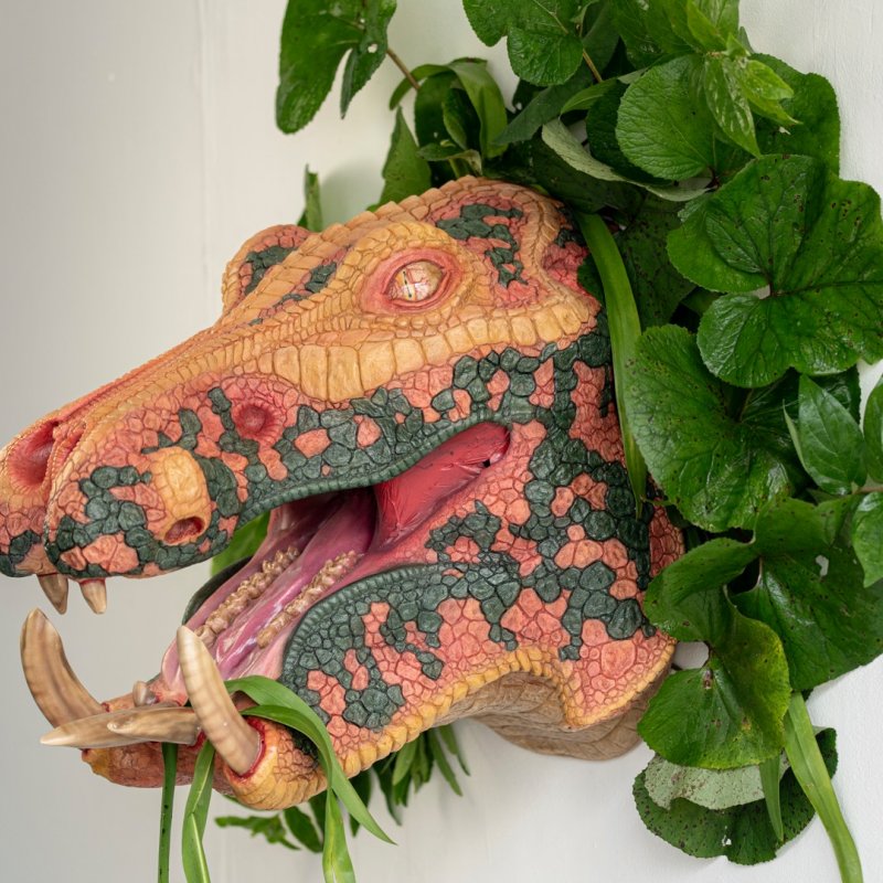 A multi-coloured velociraptor head is adorned with leafy green plants