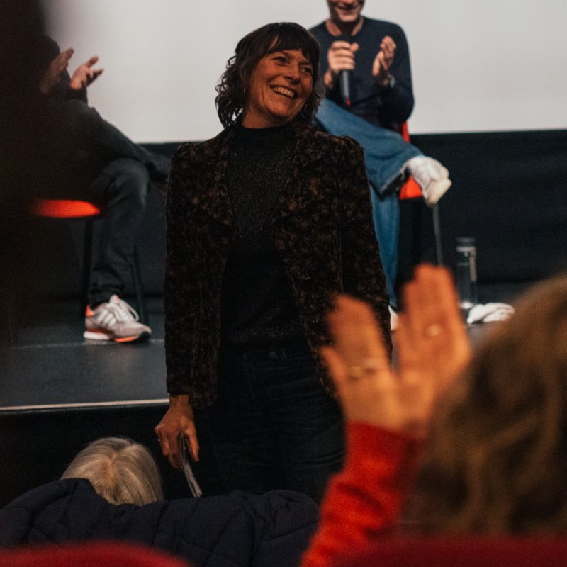 Actress Mary Woodvine being applauded by a live audience in a cinema screen