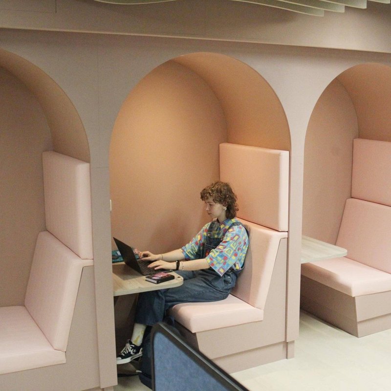 A Falmouth University student sitting in a pink alcove seat with a laptop
