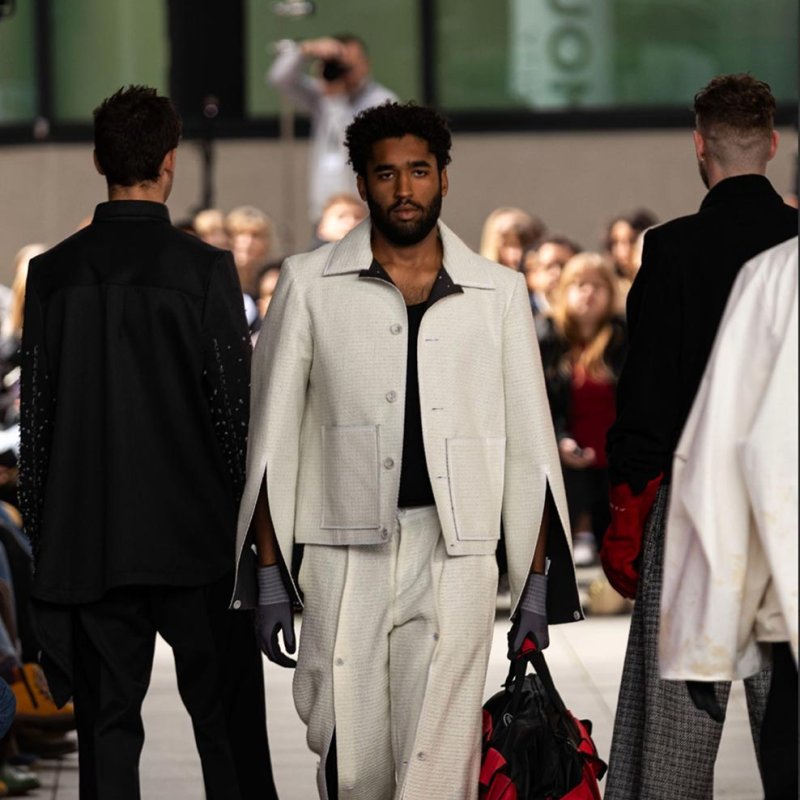 A man wearing a white suit, carrying a bag on the catwalk