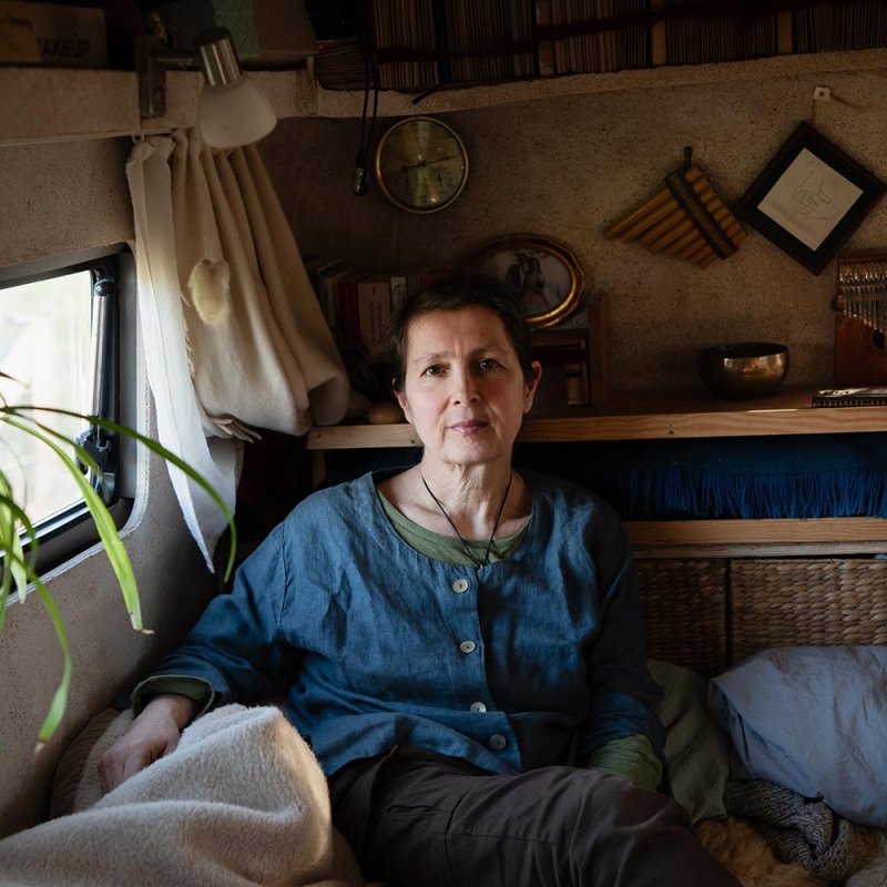 Photograph of a woman sat in a converted van with shelf and personal objects