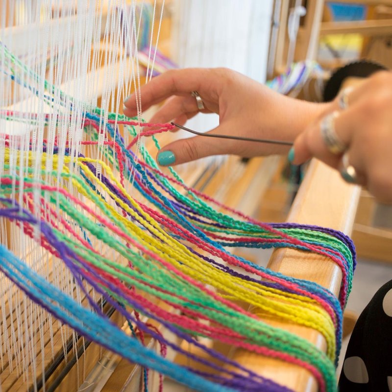 A hand using a weaving machine with multi-coloured wool