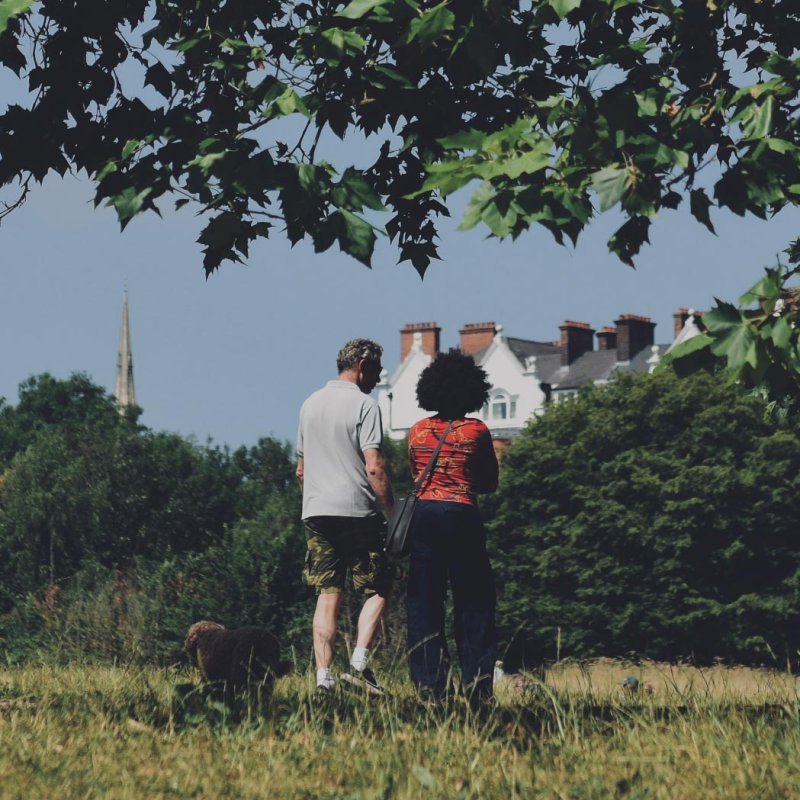Two people and a dog standing in a field by a tree