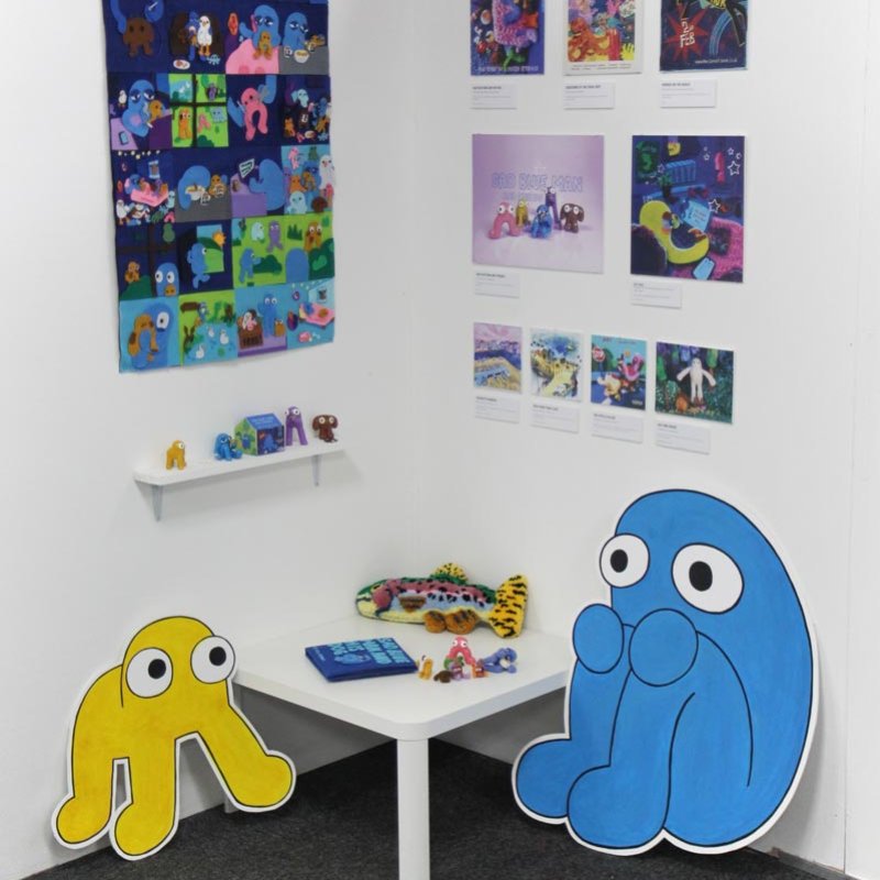 graphic work displayed on a white wall with cartoon character cutouts on the floor