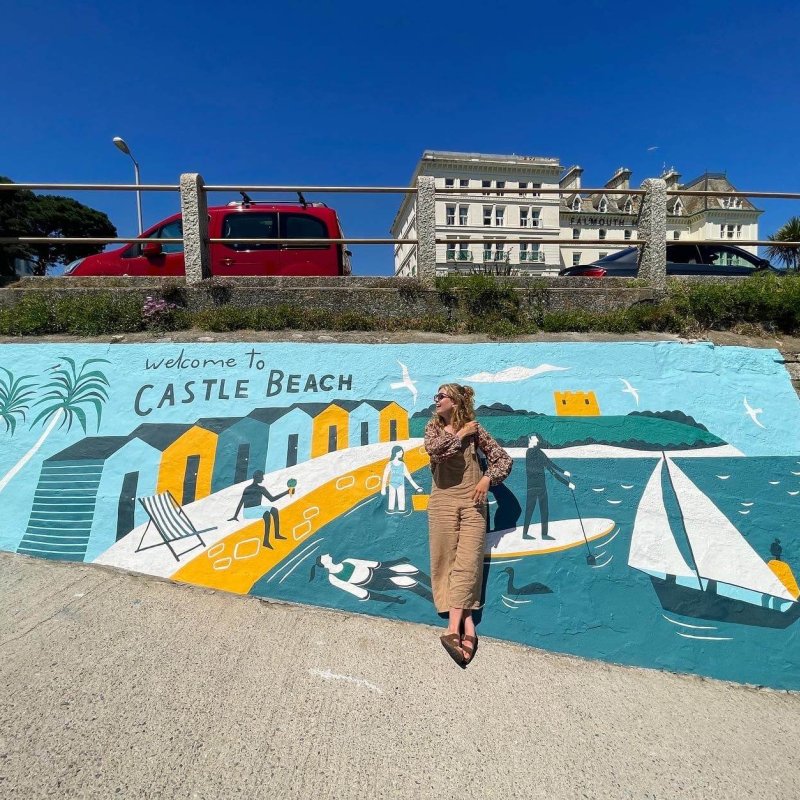 A girl standing in front of a beach-themed mural titled 'Welcome to Castle Beach'