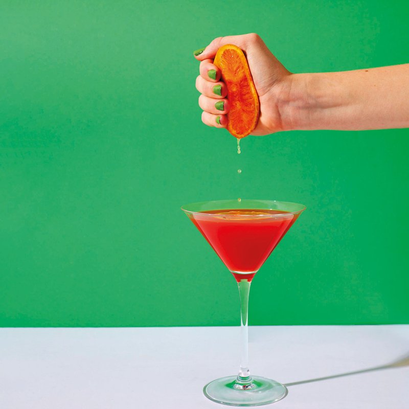 Hand squeezing fruit into cocktail