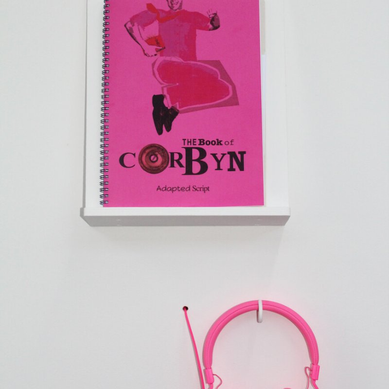Pink book called "Book of Corbyn" on display with pink headphones.