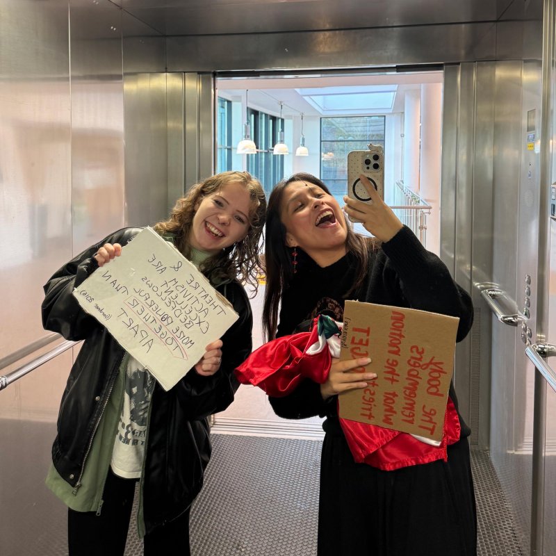 Two Theatre & Performance students smiling and holding signs